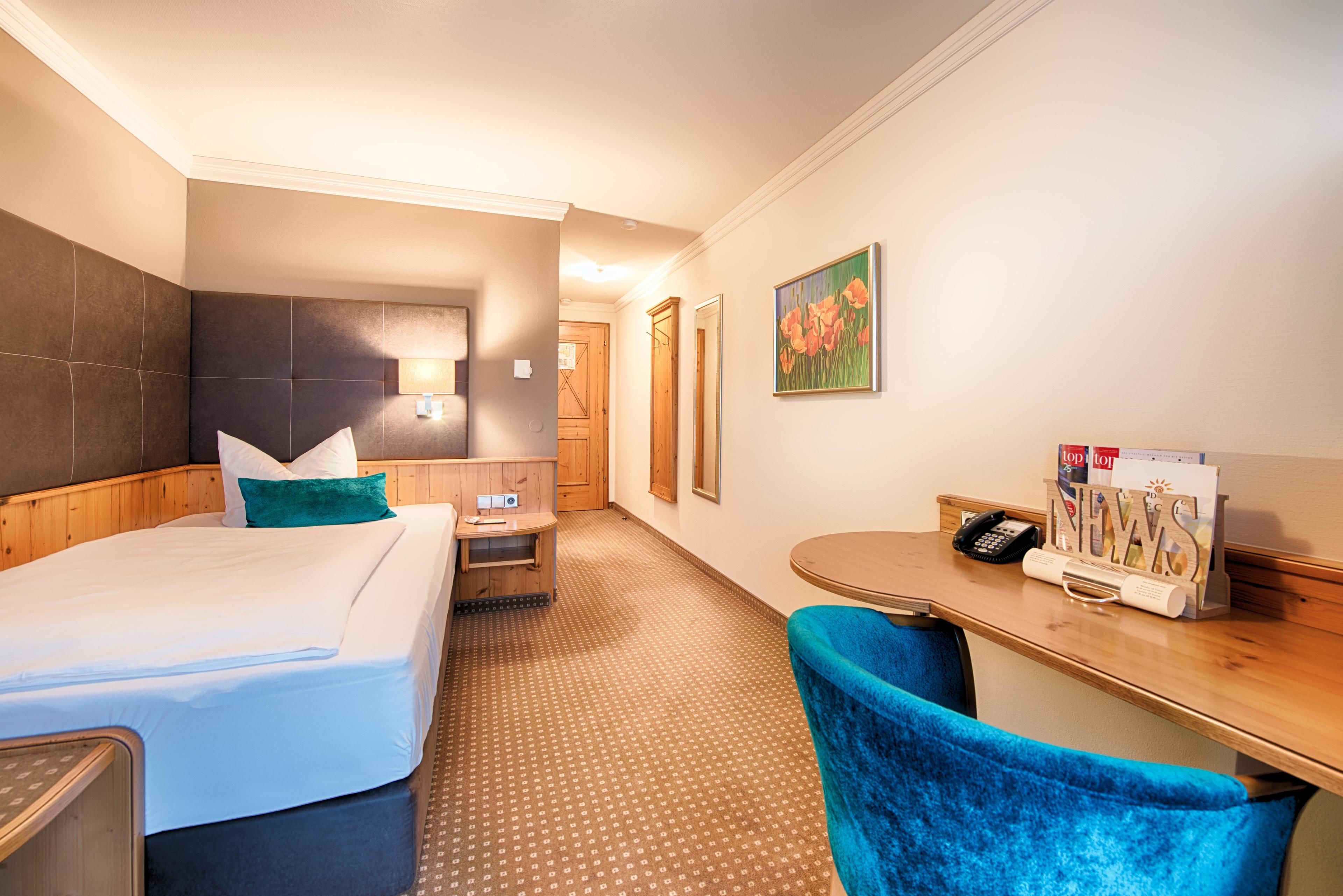 A hotel room with a bed, a desk with a telephone, a chair, and a wall-mounted TV.