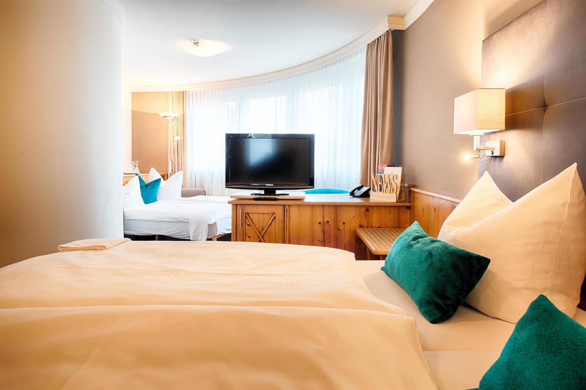 A hotel room with a large bed, a television, a desk with a chair, and a window with curtains.