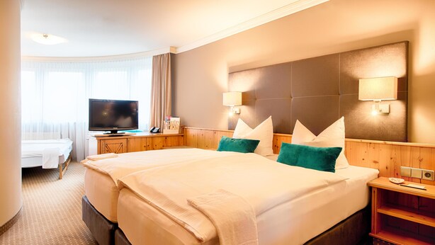 A hotel room with two beds, a TV, a desk with a chair, and a window with curtains. - Hotel Landhaus Feckl (Ehningen)