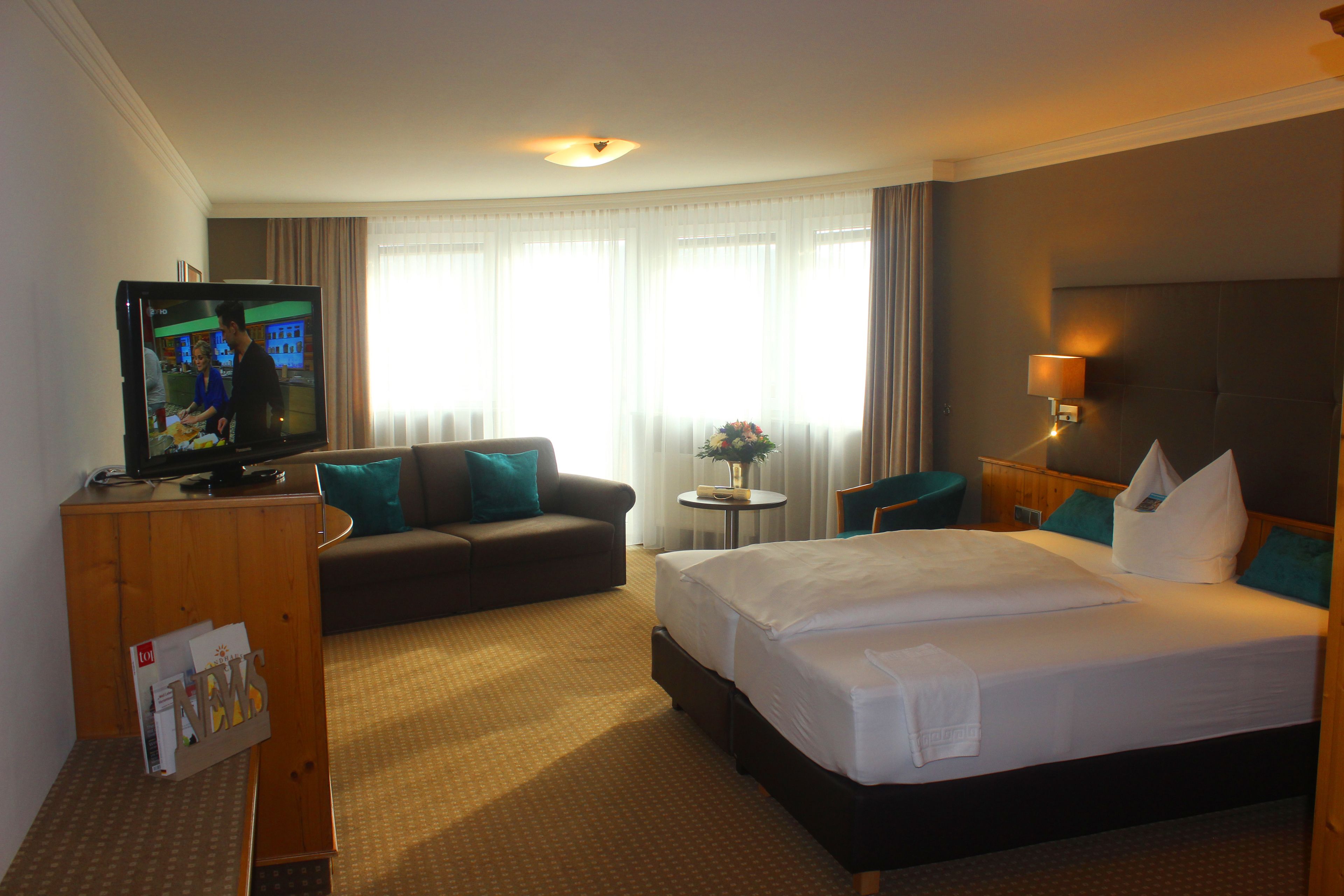 Una habitación de hotel con una cama grande, un sofá, un televisor y una mesita con un florero.