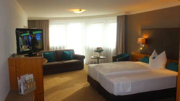 Una habitación de hotel con una cama grande, un sofá, un televisor y una mesita con un florero.