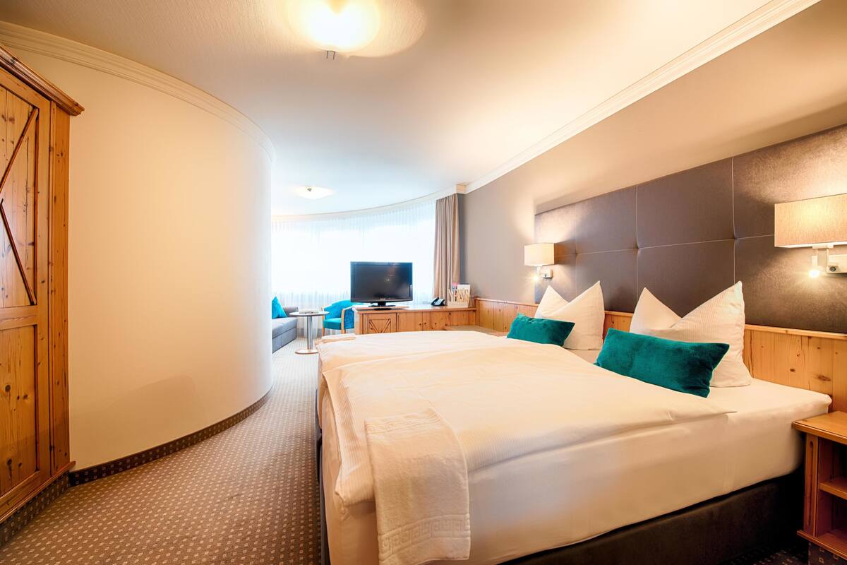 A hotel room with a large bed, a television, a desk, and a curved wall with a wooden panel.