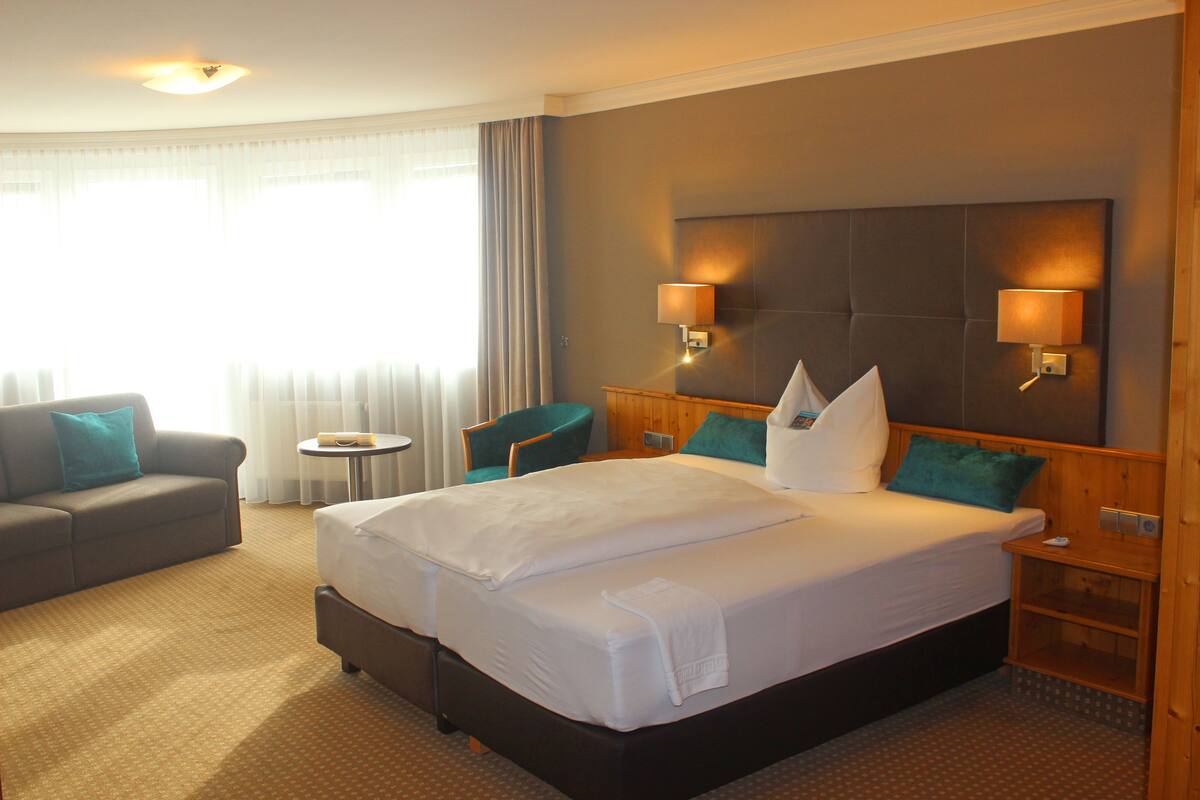 A hotel room with a large bed, a sofa, a small table, and two wall-mounted lamps.