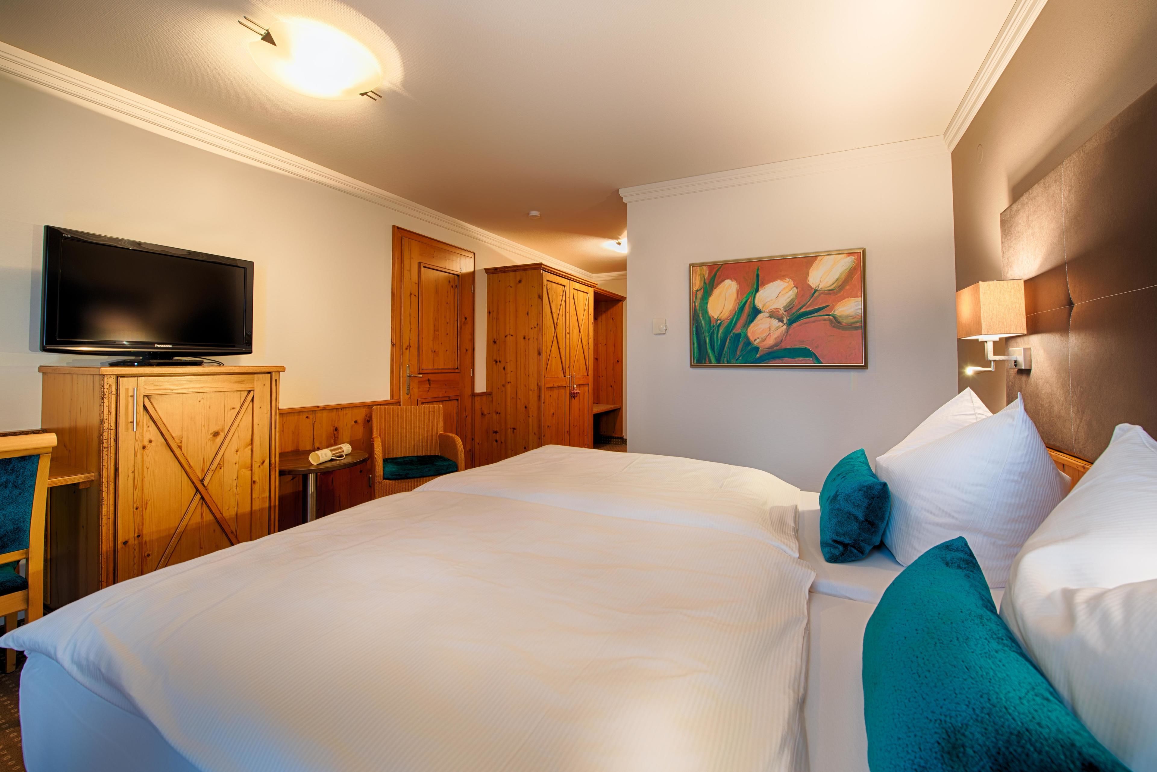 A hotel room with a large bed, a television, wooden cabinets, and a painting on the wall.