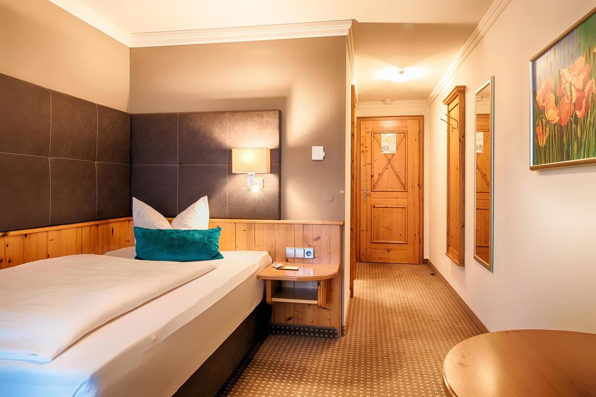 A hotel room with a bed, bedside table, lamp, and a small wooden table.