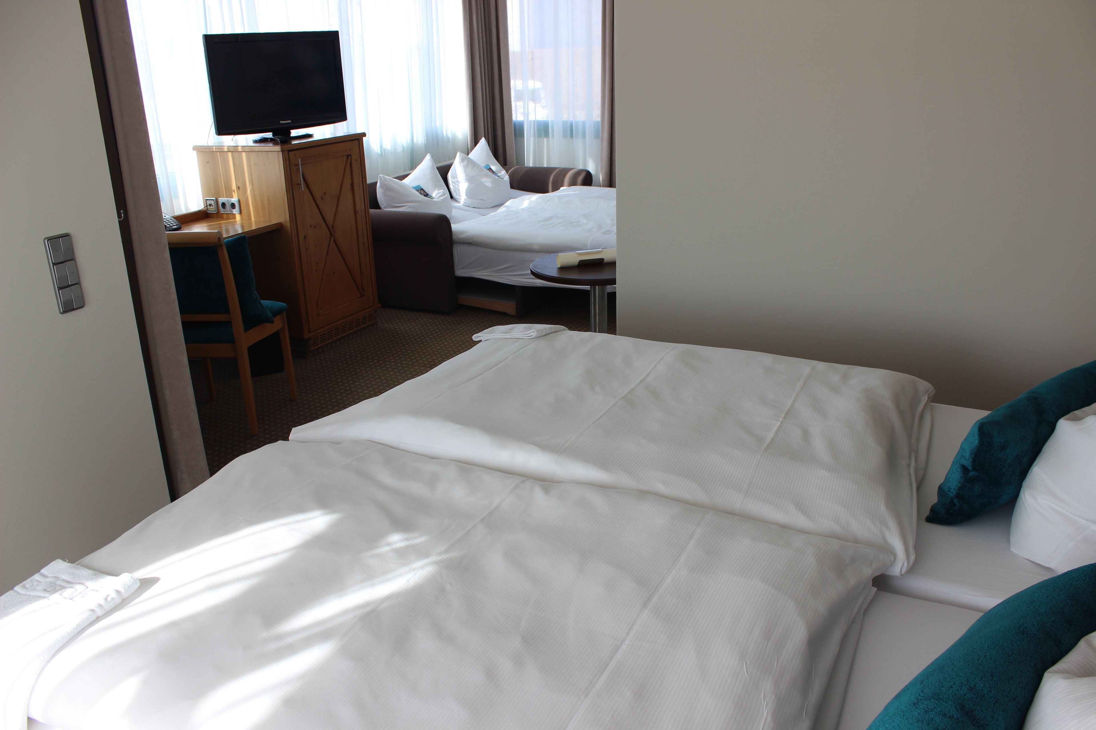 Una camera d'albergo con un letto, una scrivania con un computer, una televisione e un angolo salotto con un divano e poltrone.