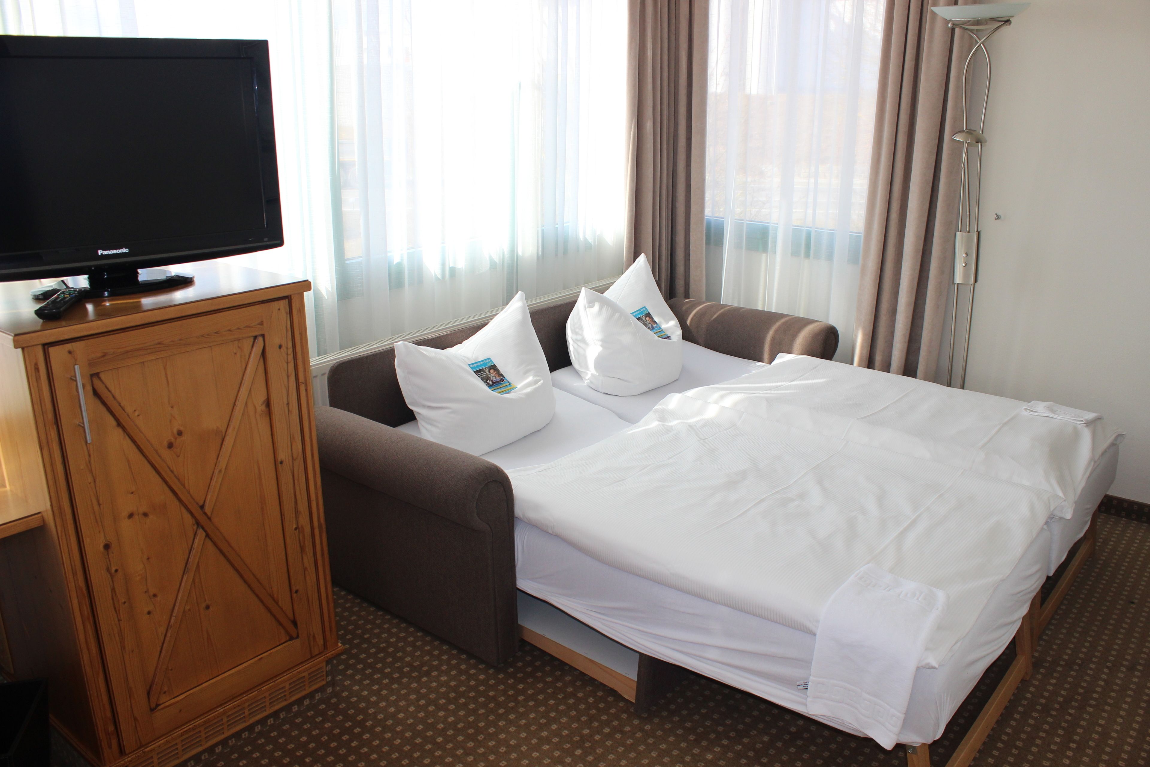 A hotel room with a bed, a television on a wooden cabinet, and a window with curtains.