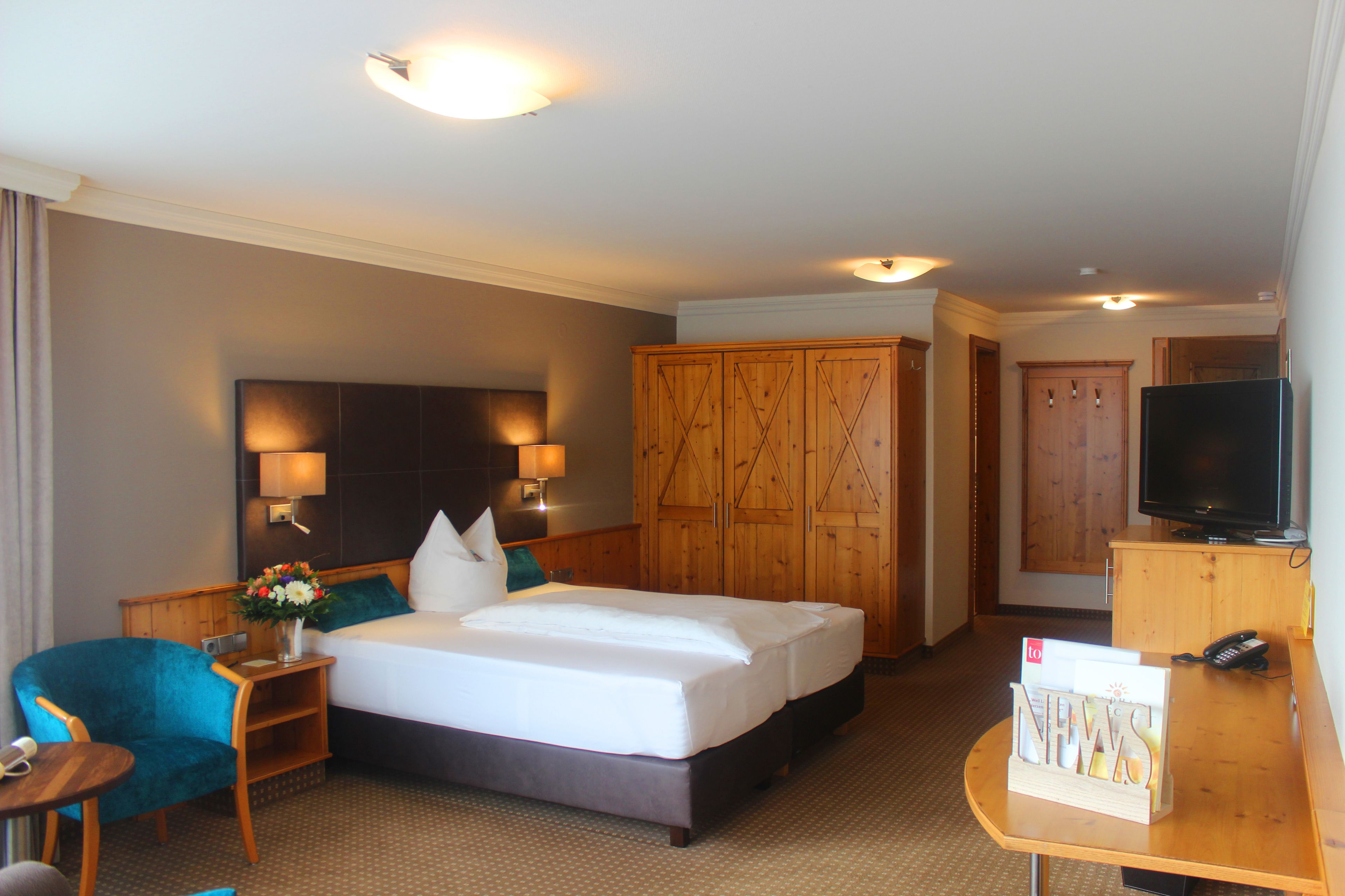 A hotel room with a bed, a desk, a chair, a television, and a wardrobe.
