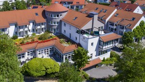 A modern residential building with multiple balconies, a central courtyard with a circular structure, and surrounding greenery. - Hotel Landhaus Feckl (Ehningen)