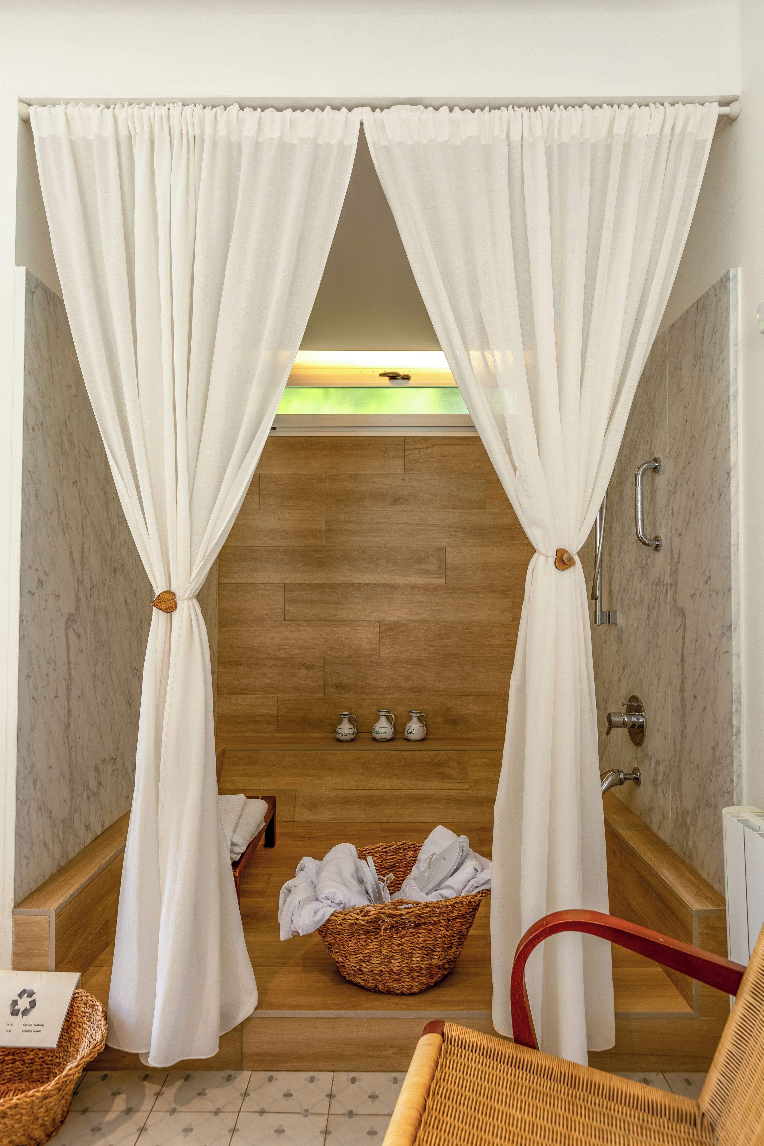 Un baño con piso de madera, una bañera, zona de ducha y una cesta de mimbre con toallas.