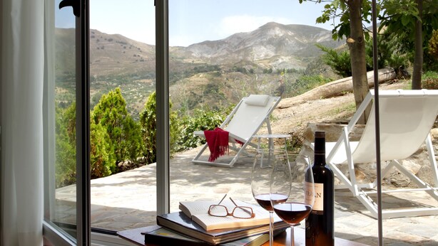 A room with a large window, a table with a wine bottle and glasses, and a view of the outdoors. - La Almunia del Valle (Monachil)
