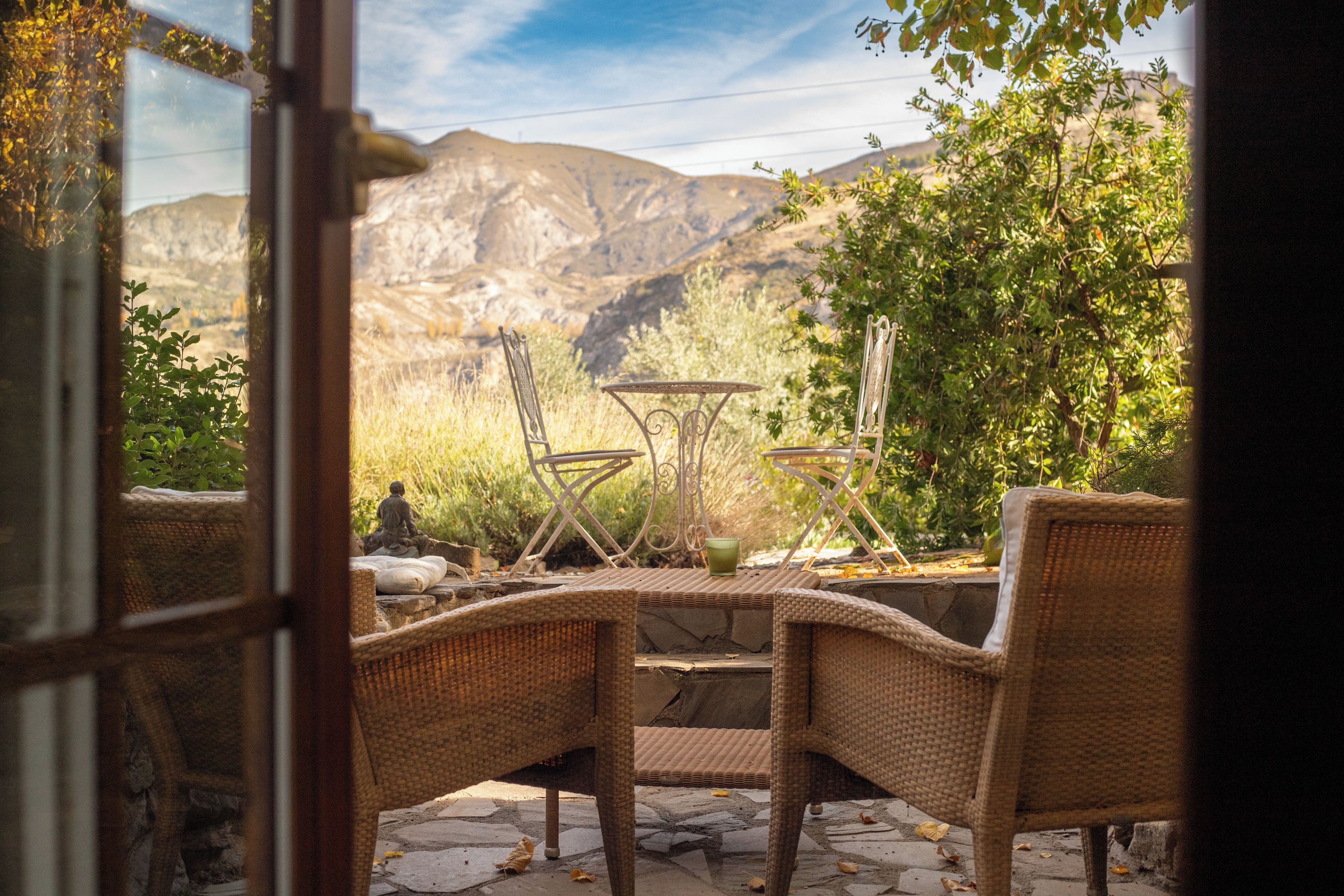 An outdoor seating area with wicker chairs and a table, overlooking a mountainous landscape.