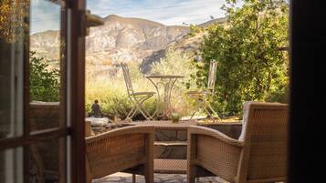An outdoor seating area with wicker chairs and a table, overlooking a mountainous landscape.