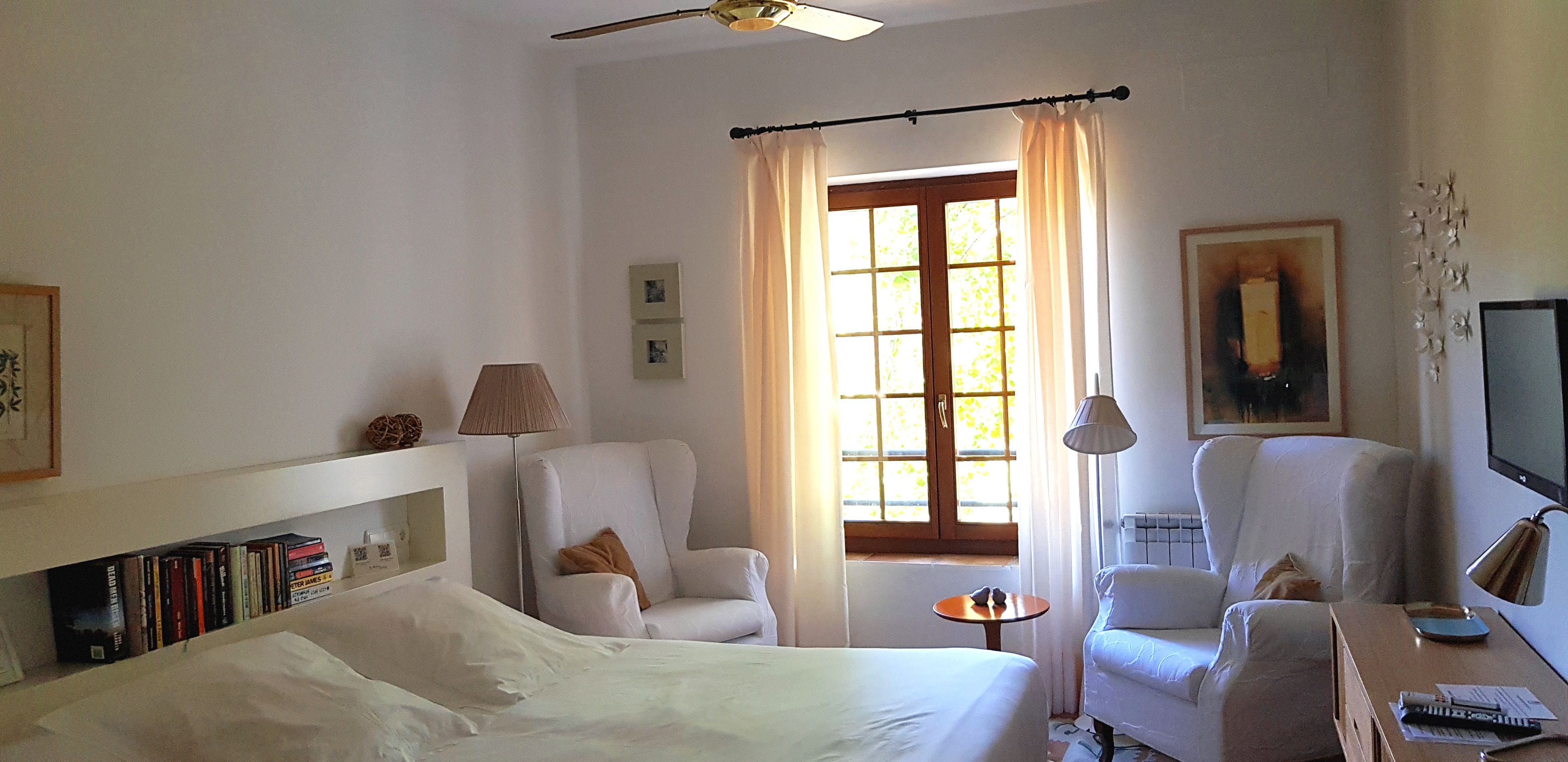 A hotel room with a bed, two armchairs, a small table, a TV, and a window with curtains.