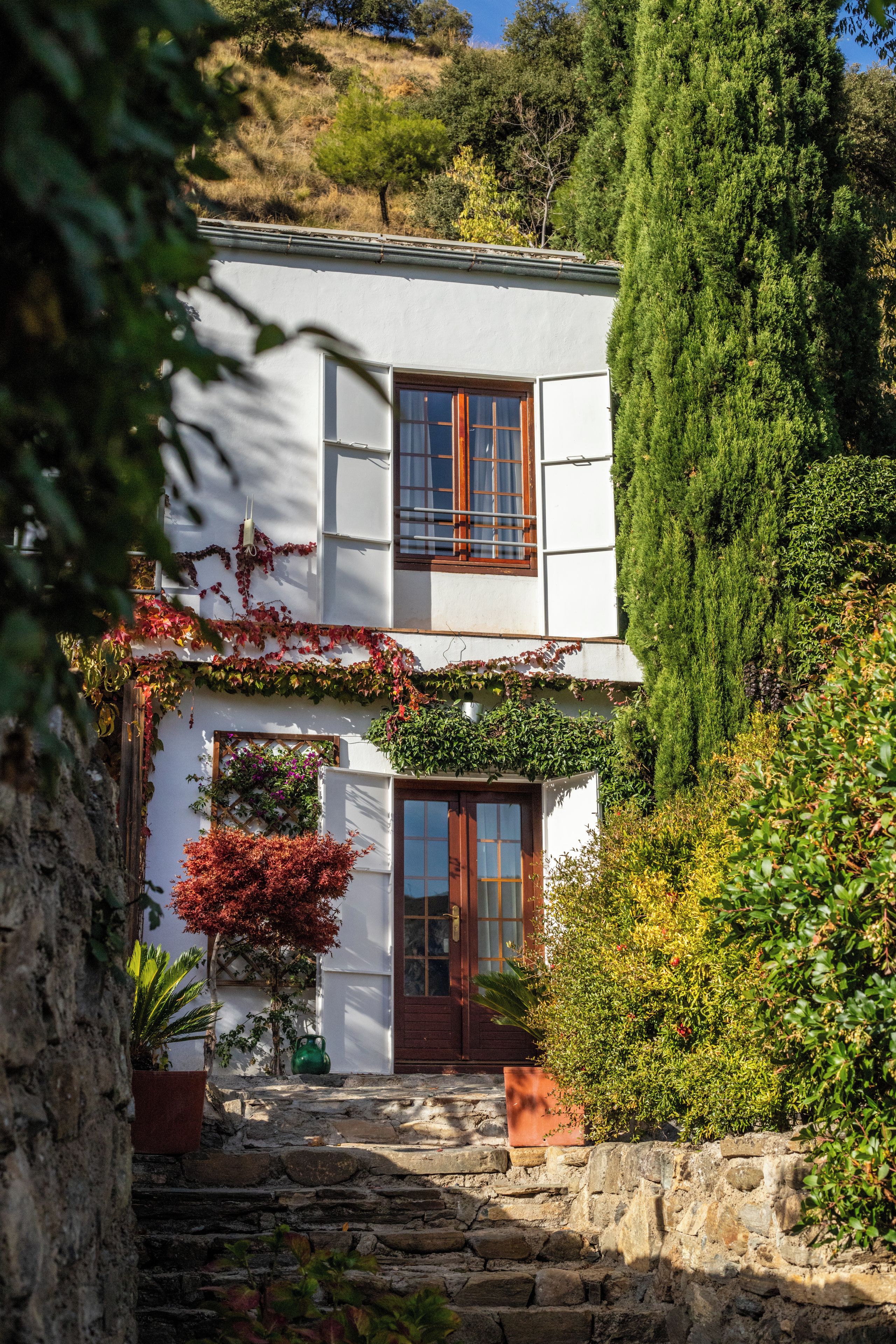Edifici de dues plantes amb façana blanca, marc de finestres de fusta i escales de pedra que condueixen a l'entrada.