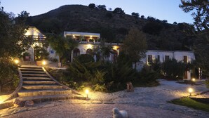 A well-lit building with a staircase leading to a balcony, surrounded by trees and a hilly landscape. - La Almunia del Valle (Monachil)