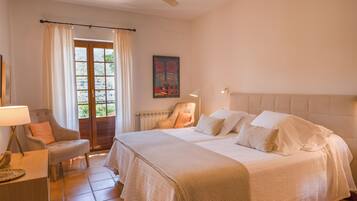 A bedroom with a double bed, a chair, a desk, and a window with curtains.
