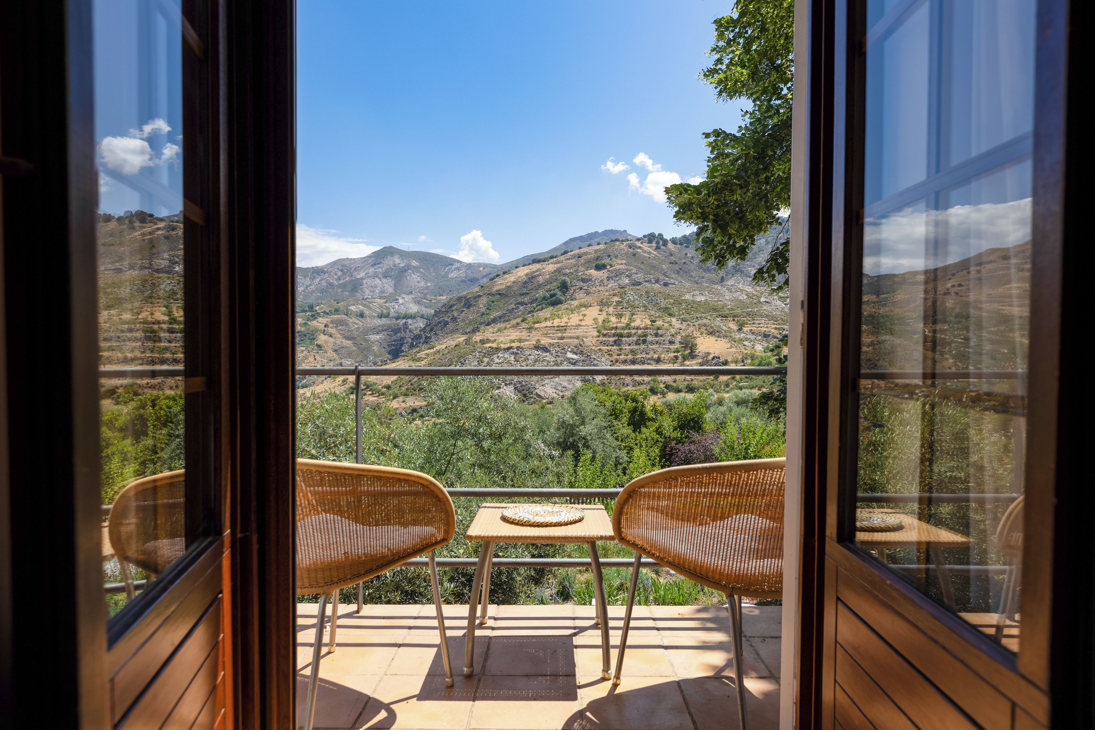 Un balcon agrémenté de fauteuils en osier et d’une petite table, offrant une vue sur un paysage montagneux.