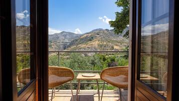 Un balcon agrémenté de fauteuils en osier et d’une petite table, offrant une vue sur un paysage montagneux.