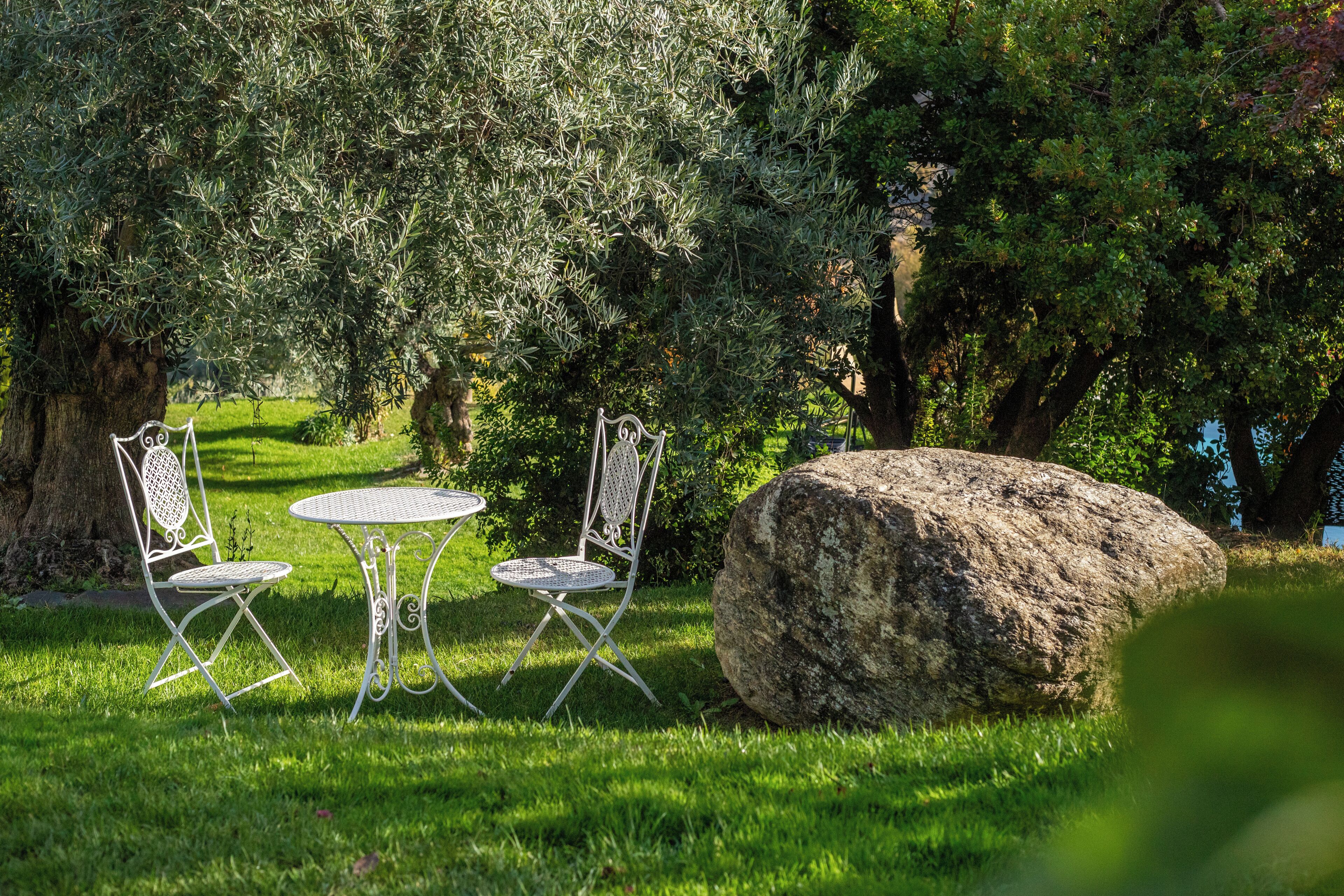 Un jardin avec une table et des chaises, un grand rocher et des arbres.