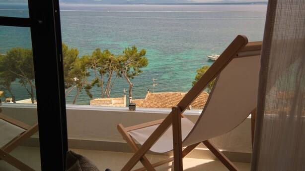 Un balcón con vista al mar, una silla de madera y una barandilla.