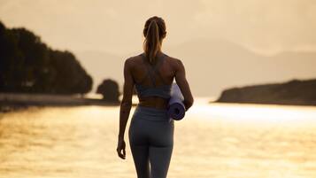 Una persona caminando sobre la playa con una esterilla de yoga, usando un top deportivo y leggings.