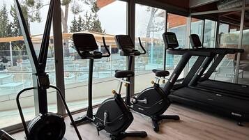 A gym with exercise equipment, large windows, and a wooden ceiling.