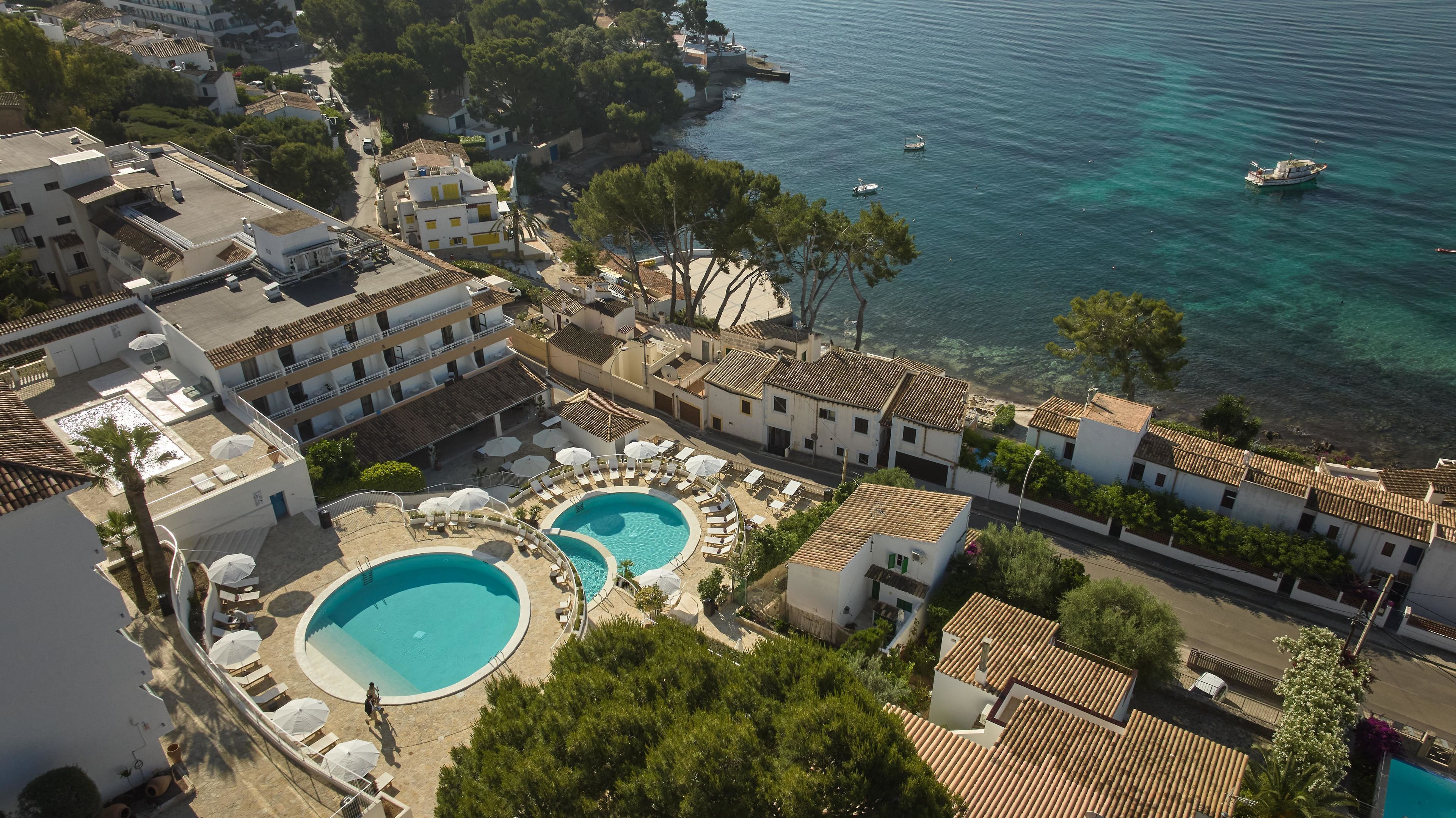 A coastal hotel with two swimming pools, a beach, and a view of the sea.