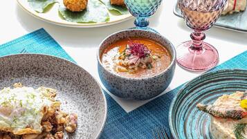 Una mesa dispuesta con diversos platos, incluyendo un tazón de sopa, una rebanada de pan y un plato con carne y verduras.