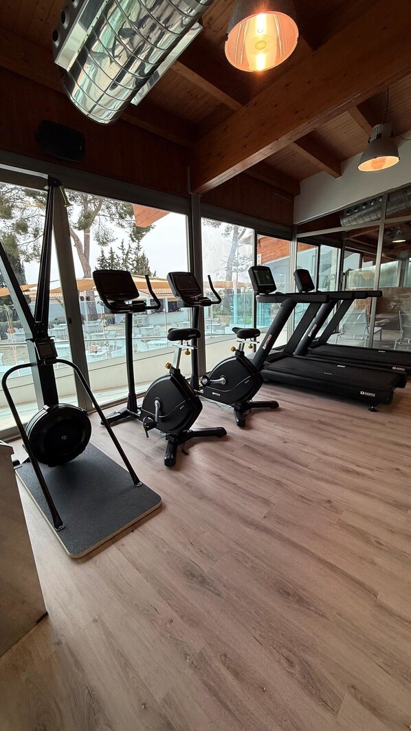 A gym with exercise equipment, large windows, and wooden flooring.