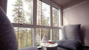 A cozy room with a large window, a small round table, and grey upholstered seating. - Tree Hotel (Harads)