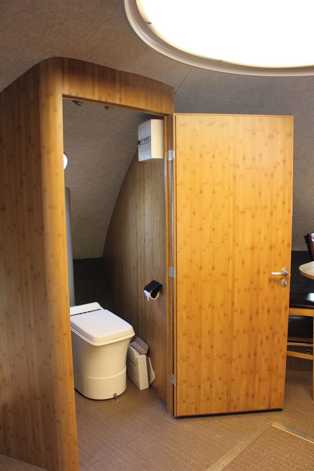 A compact wooden room with a toilet, a small trash bin, and a door.