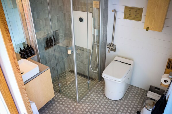 A bathroom with a glass-enclosed shower, a toilet, and a sink. - Tree Hotel (Harads)