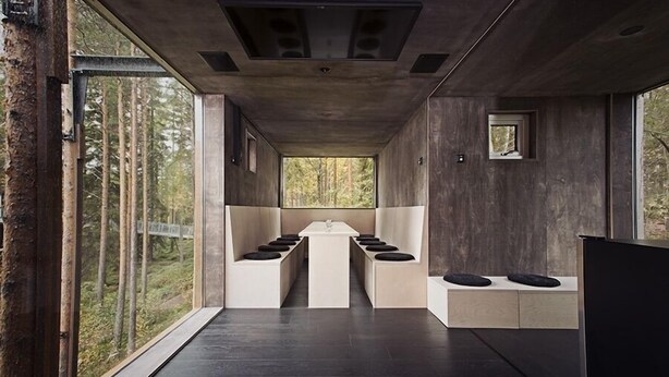 A modern interior with a long table and benches, large windows, and a view of the forest. - Tree Hotel (Harads)