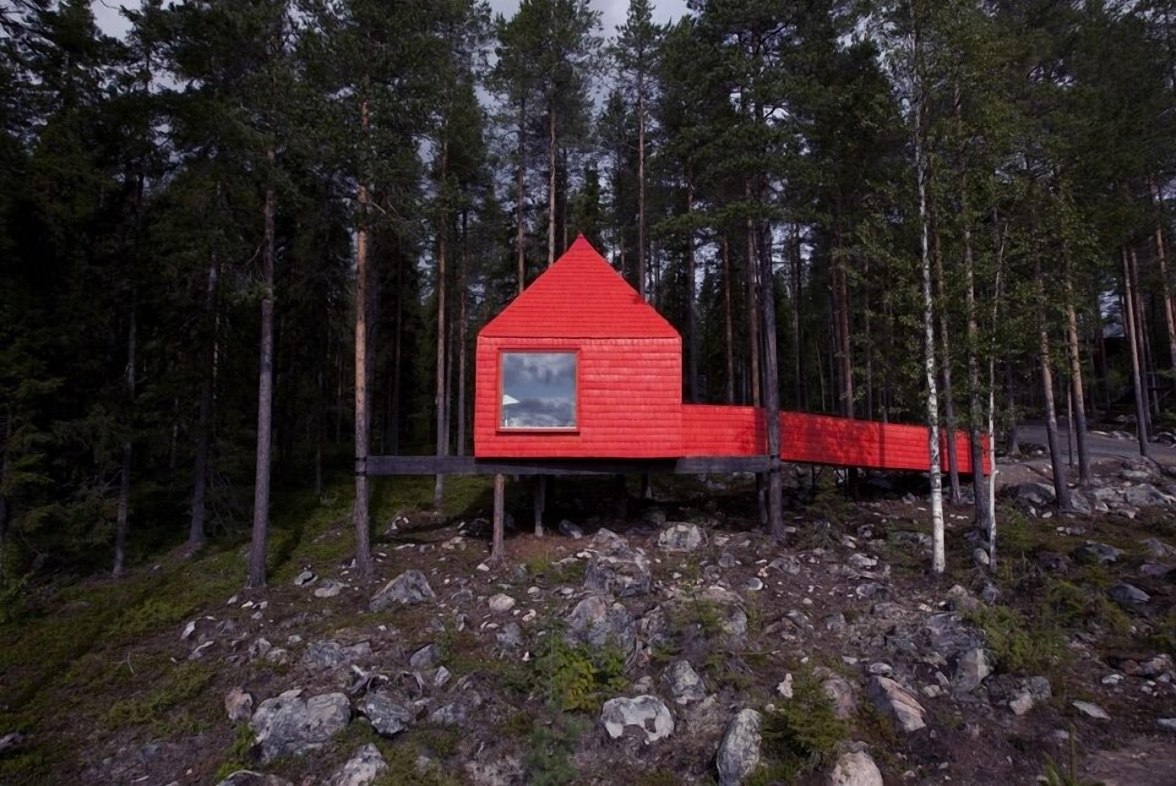 A red cabin with a triangular roof, surrounded by a forest.