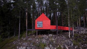 A red cabin with a triangular roof, surrounded by a forest.