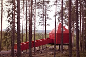 A red wooden structure in a forest with a red bridge leading to it.