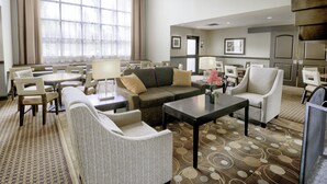 A hotel lobby with a seating area, a sofa, chairs, a coffee table, and a large window with curtains. - Staybridge Suites West Edmonton by IHG (Edmonton)