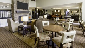 A spacious hotel lobby with a fireplace, comfortable seating, and a kitchen area in the background. - Staybridge Suites West Edmonton by IHG (Edmonton)