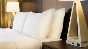 A neatly made bed with white linens, a bedside table with a lamp, and a wall-mounted light fixture. - Staybridge Suites West Edmonton by IHG (Edmonton)