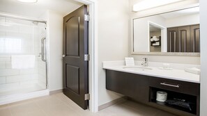 A modern bathroom with a glass shower enclosure, a dark wooden door, a white vanity with a mirror, and a towel rack. - Residence Inn by Marriott Edmonton West (Edmonton)