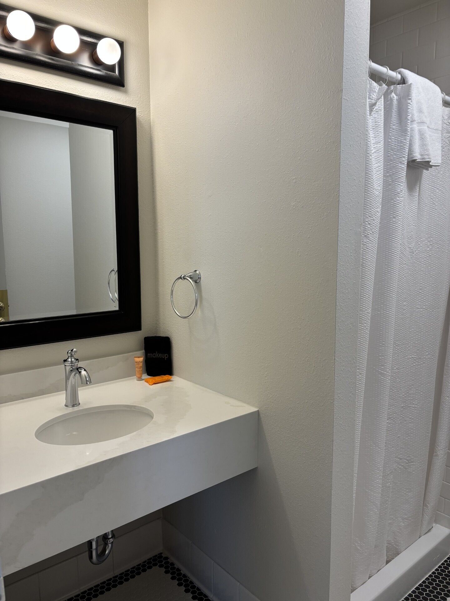 Une salle de bain avec un lavabo blanc, un miroir, un anneau lumineux au-dessus du miroir, un porte-serviettes et un rideau de douche.