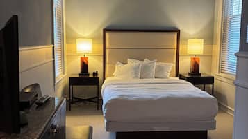 Una habitación de hotel con cama, mesitas de noche con lámparas, escritorio con televisor y una silla.