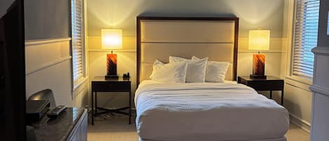 A hotel room with a bed, bedside tables with lamps, a desk with a TV, and a chair.