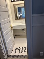 Un baño con lavamanos blanco, un espejo encima y piso con diseño hexagonal.