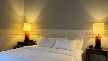 A hotel room with a large bed, two bedside tables with lamps, and a plain wall.