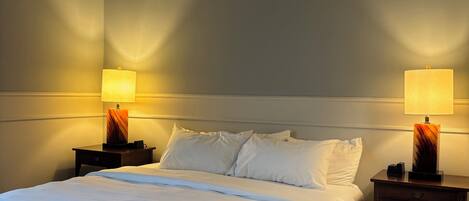 A hotel room with a large bed, two bedside tables with lamps, and a plain wall.