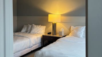 A hotel room with two beds, a nightstand with a lamp, a tissue box, and a power outlet.