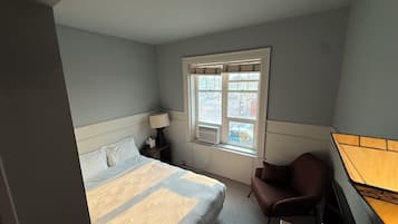 Una habitación de hotel con cama, una silla, un escritorio y una ventana con persianas.