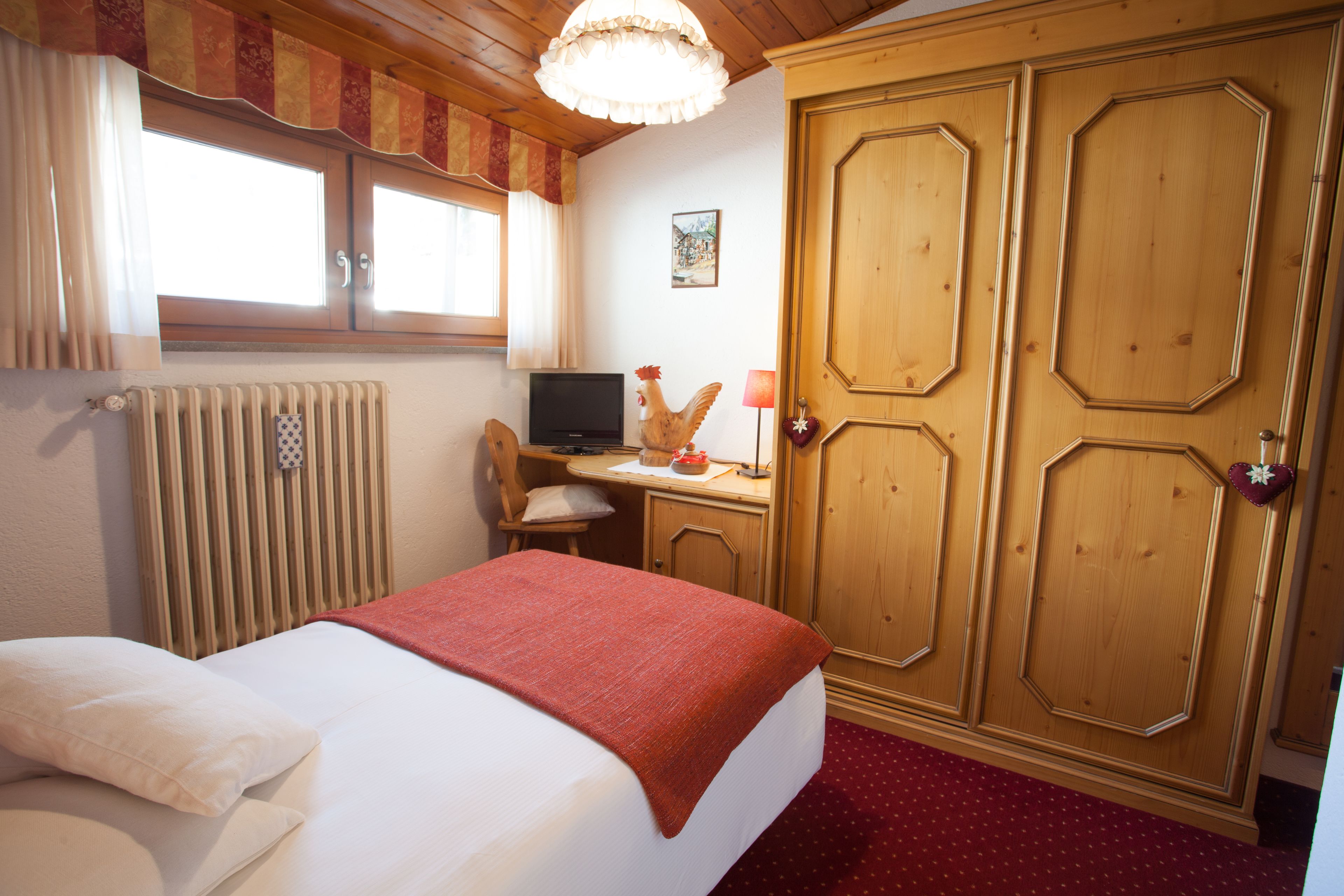 A bedroom with a bed, a desk with a computer, a radiator, and wooden wardrobes.